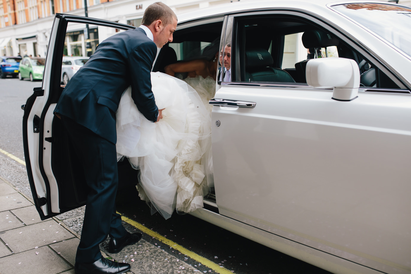 Helping the bride into the car. Documentary wedding photography